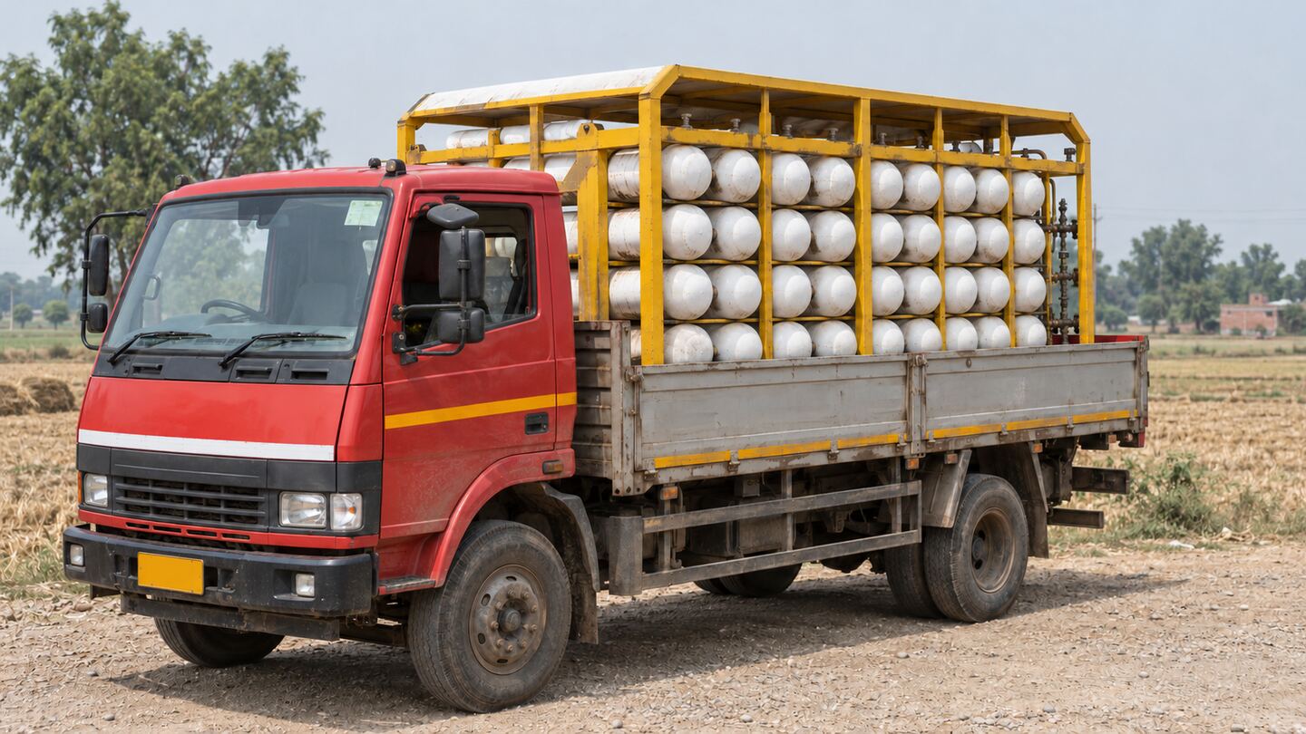 A truck carrying a cascade of horizontal compressed-gas cylinders on a rural road between fields in north India